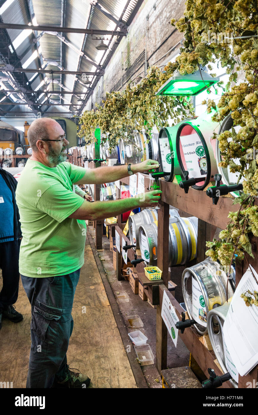 Inghilterra, Tunbridge Wells. CAMRA la birra e il festival ale. Uomo maturo permanente e la colata di una pinta di birra dalla canna, tra i filari di vari barili di birra. Foto Stock