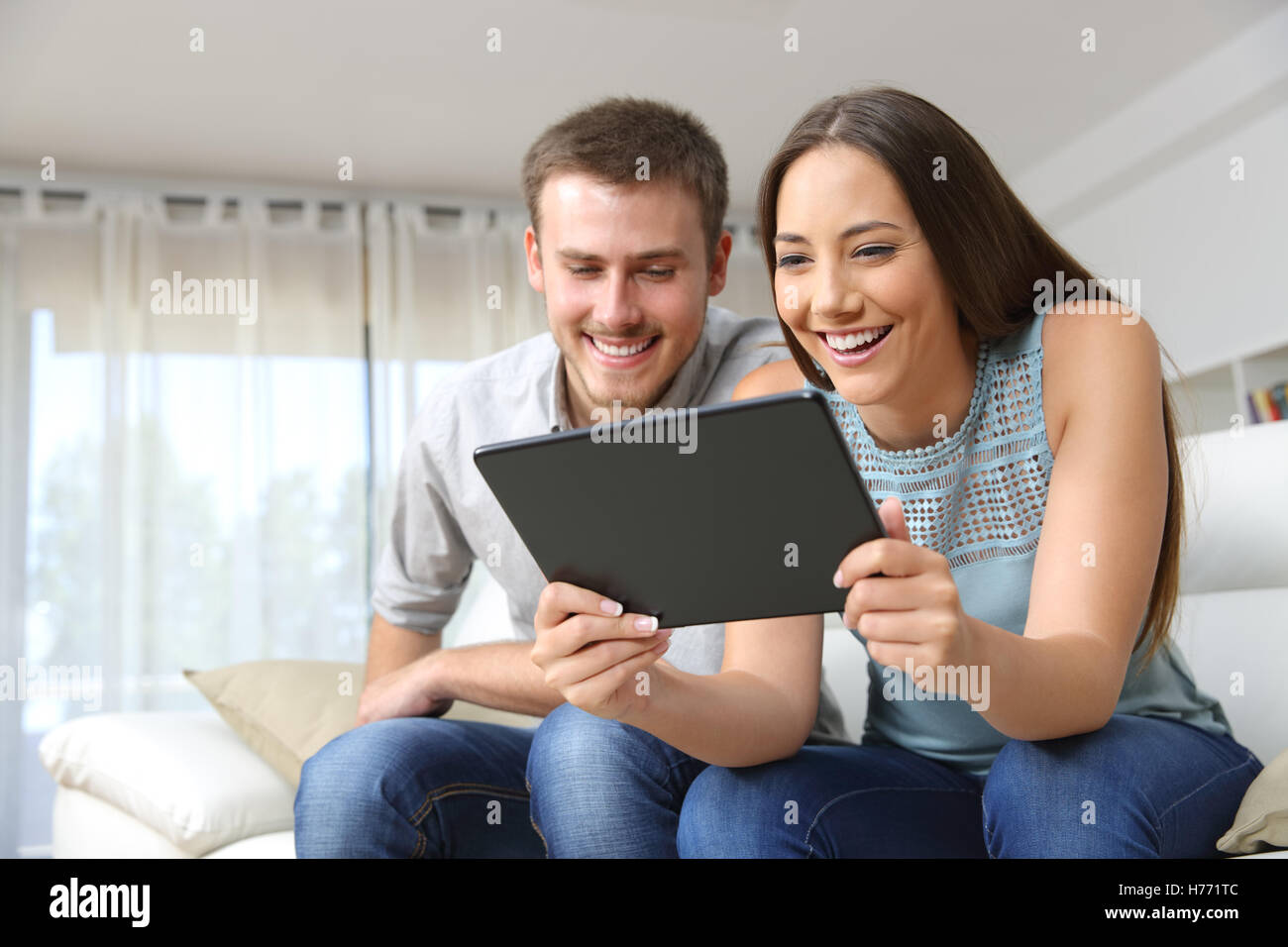Paio di godersi i contenuti multimediali in un tablet seduto su un divano nel soggiorno in un interno di una casa Foto Stock
