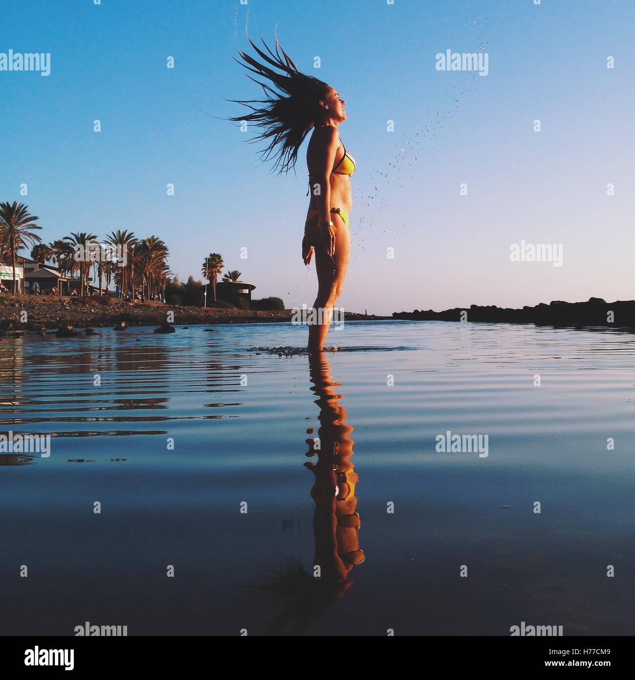 Donna in piedi in oceano la bagnatura e capovolgendo i suoi capelli Foto Stock