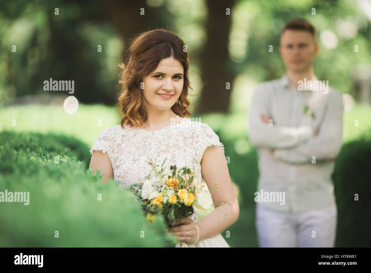 Sposa in posa e sorrisi mentre lo sposo attende sullo sfondo Foto Stock
