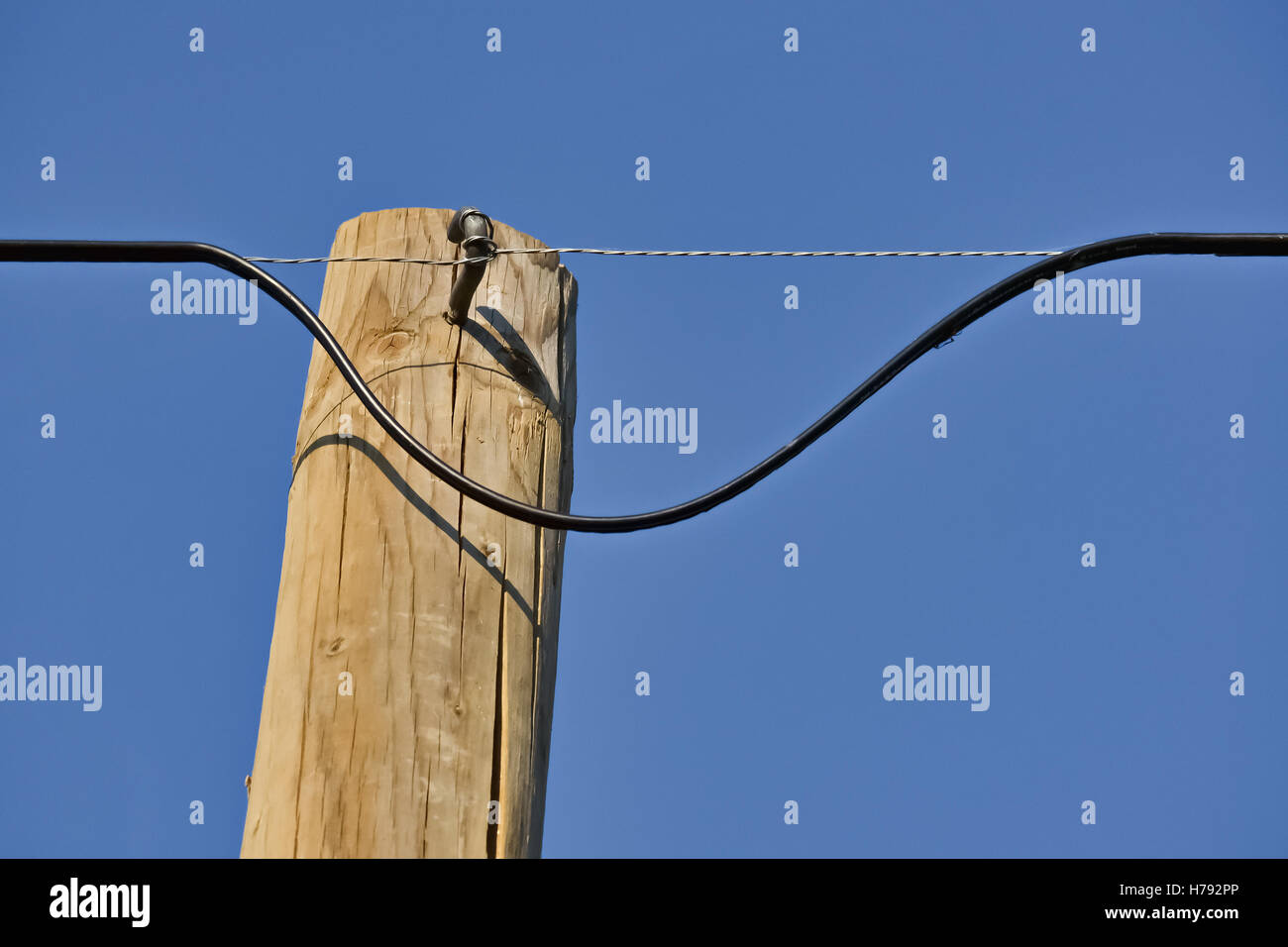 Primo piano della pericolosità di un cavo elettrico su un traliccio di legno e il cielo chiaro Foto Stock