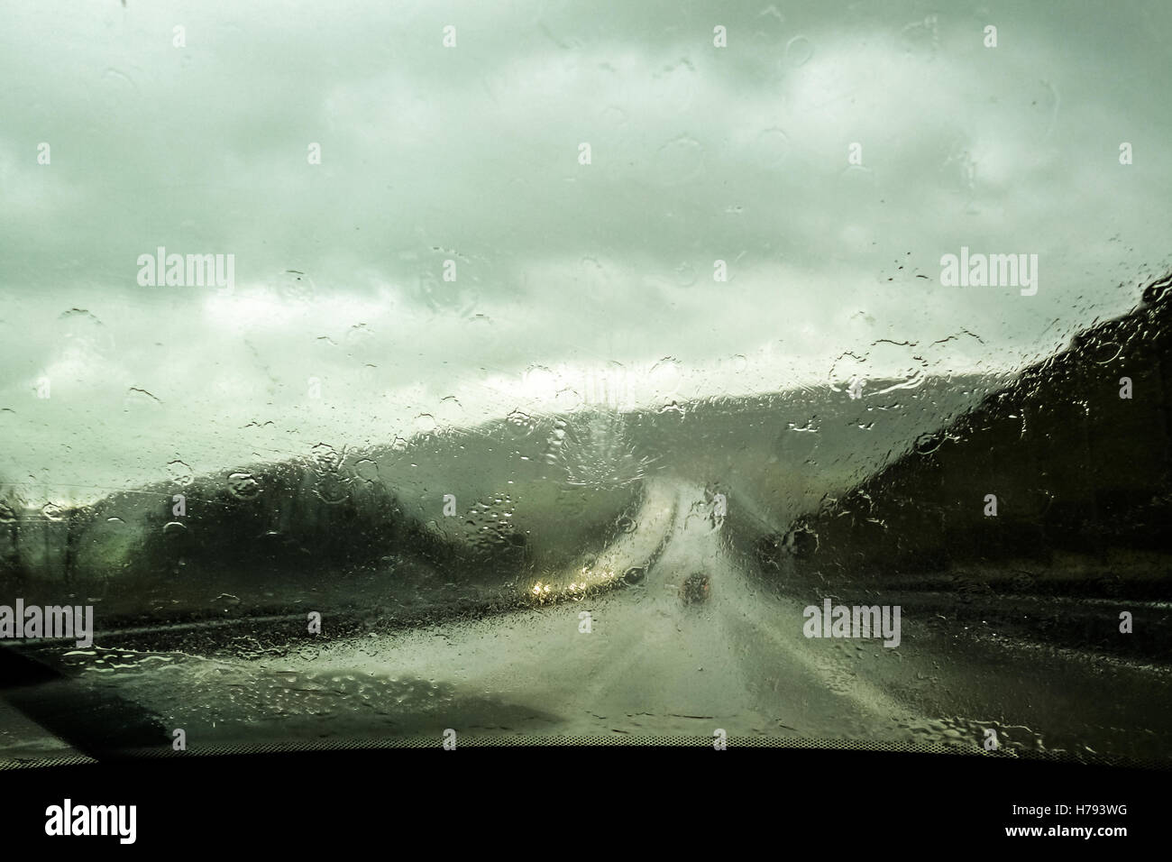 Finestra anteriore della vettura sotto la pioggia. Vista dalla vettura del sedile anteriore sulla lunga strada davanti durante la pioggia le gocce di pioggia sulla finestra Foto Stock