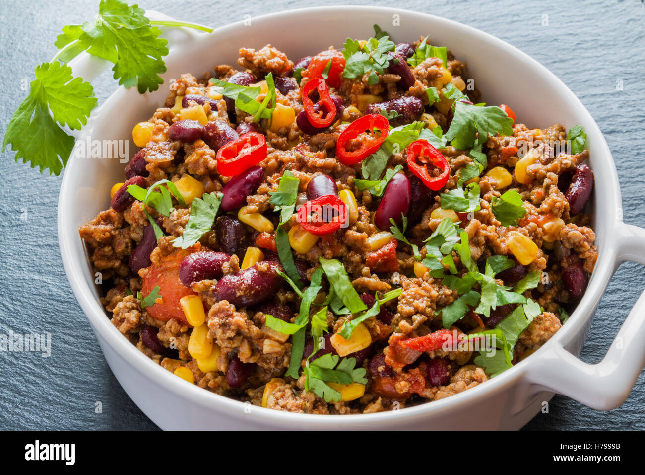 Chili con carne in una casseruola di bianco su nero lo sfondo di pietra. Cucinato con carne di manzo macinata, pomodori, peperoni, fagioli, mais, aglio, Foto Stock