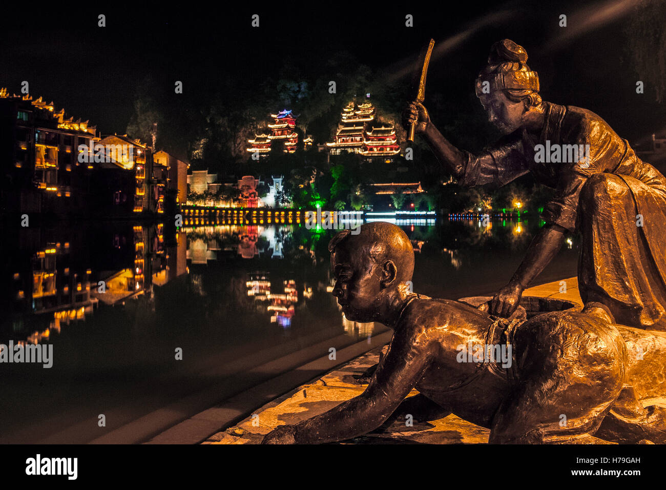 Sculture in bronzo e il fiume Wuyang da notte e sullo sfondo le luci di Zhenyuan e il Drago Nero Grotta. Guizhou (Cina) Foto Stock