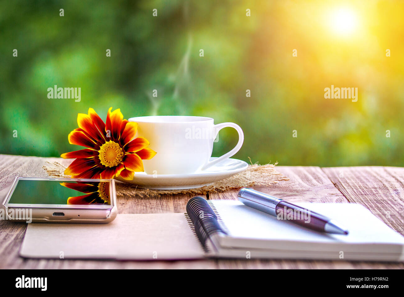 Vuoto notebook bianco, fiori e la tazza di caffè sulla scrivania all'aperto in estate Foto Stock
