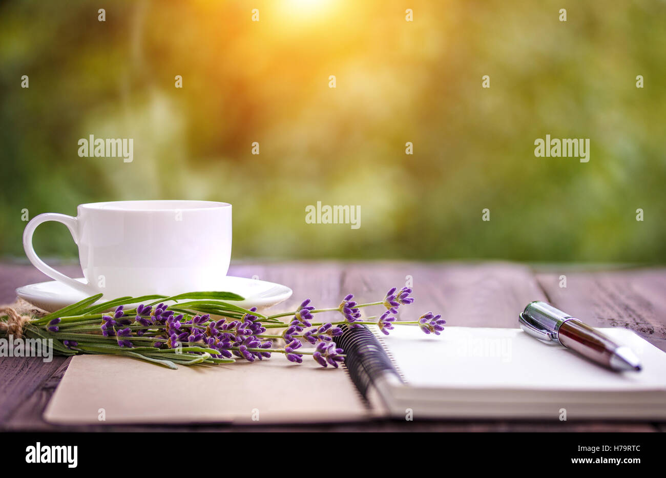 Vuoto notebook bianco, fiori e la tazza di caffè sulla scrivania all'aperto in estate Foto Stock