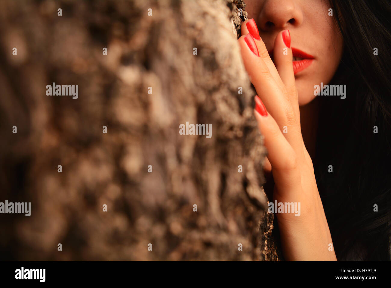 Ragazza dietro ad un albero che mostra solo la sua bocca, il naso e una mano Foto Stock