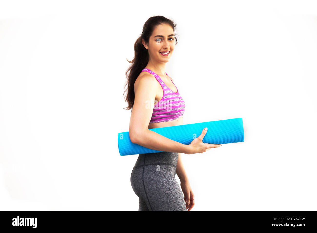 Giovane bella donna caucasica nel trasporto di abbigliamento sportivo materassino yoga in bianco sullo sfondo isolato Foto Stock