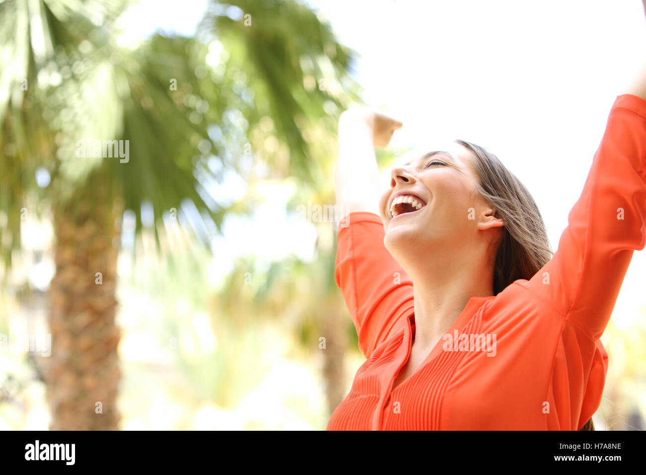 Ritratto di una donna eccitata con gli occhi chiusi i bracci di sollevamento skyward all'aperto con palme in background Foto Stock