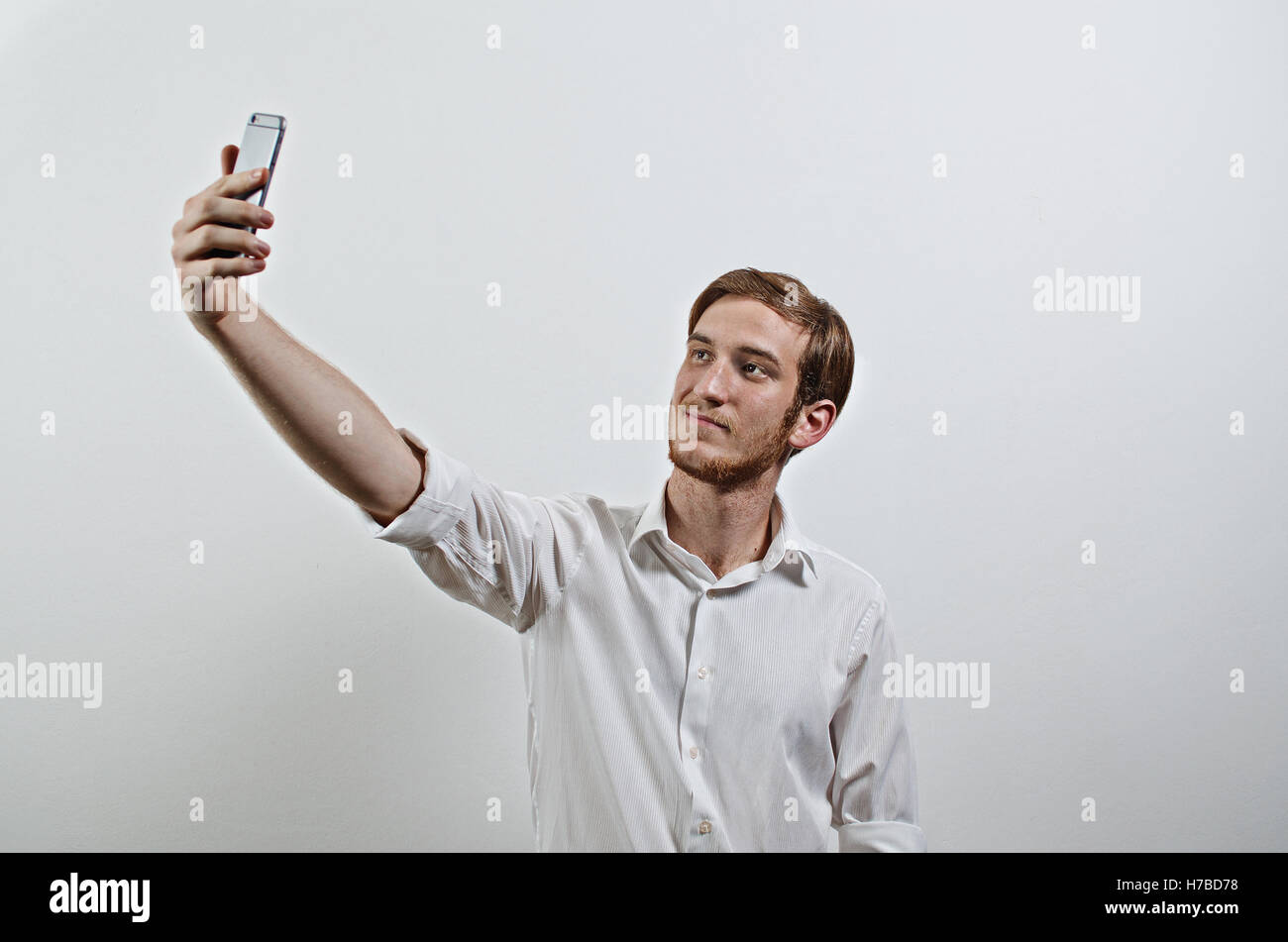 Giovane Adulto Uomo in camicia bianca si prende un Selfie con il suo telefono cellulare Foto Stock