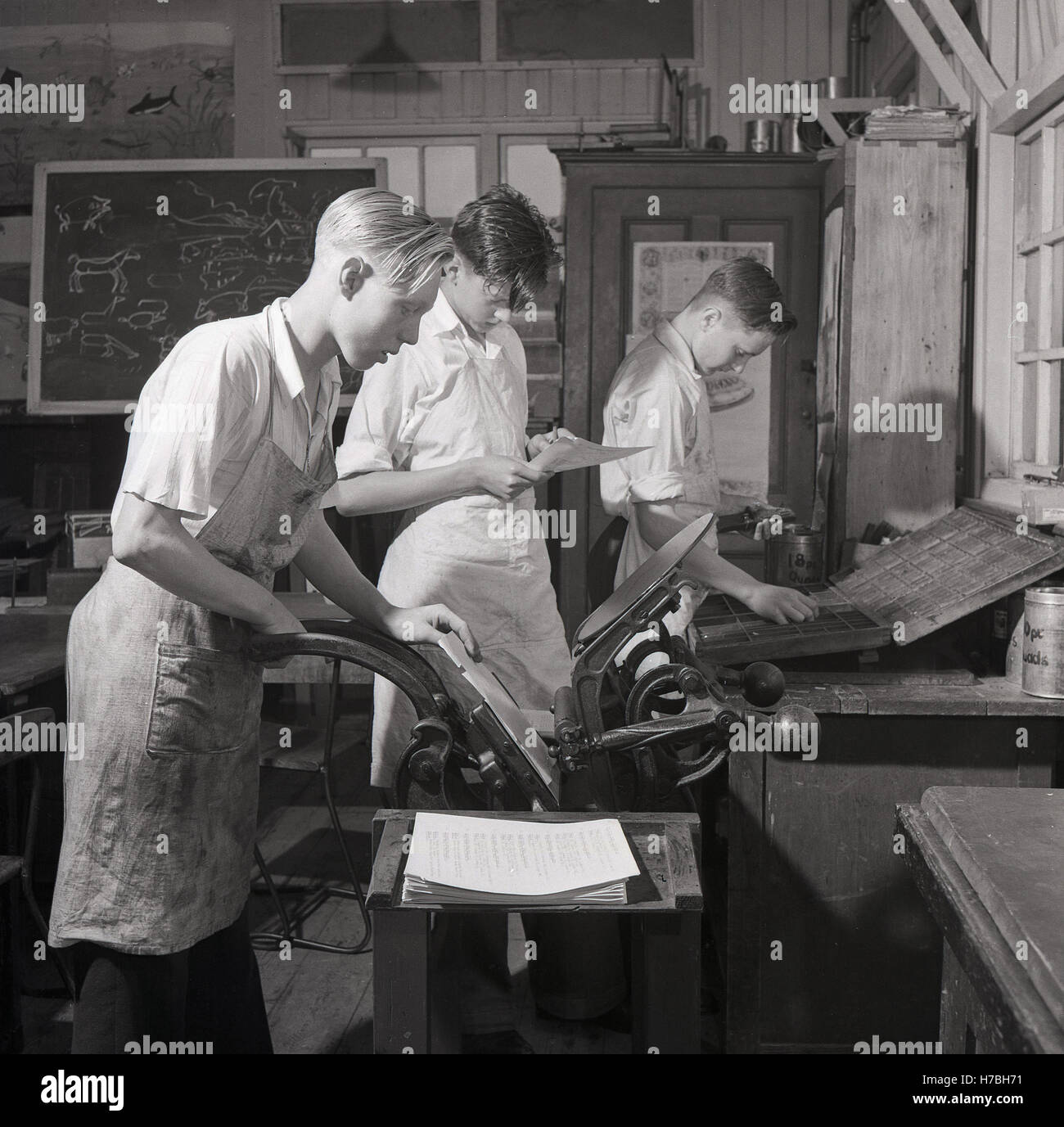 Degli anni Cinquanta, storico, Londra, Inghilterra. Maschi giovani apprendisti in un laboratorio di stampa, uno utilizzando una pressa manuale per stampa tipografica stampa, un altro assemblaggio di tipo metallico in parole e linee con una composizione di stick. Foto Stock