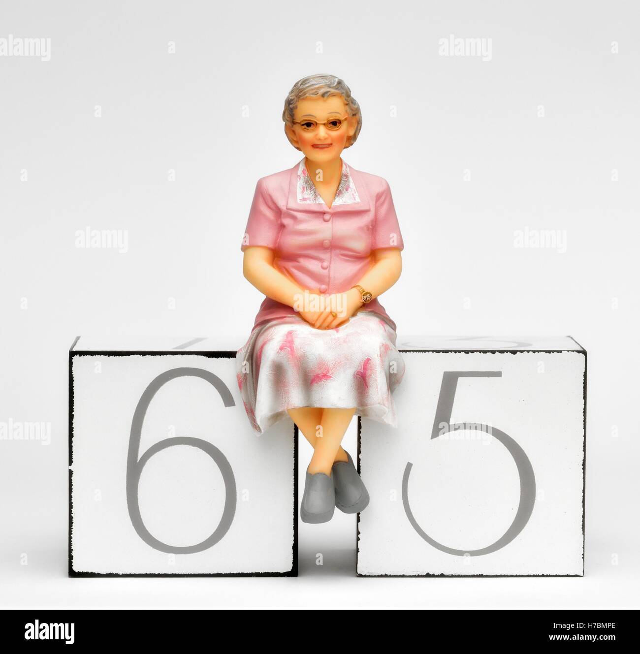 Una statuetta femminile seduta titolare di pensione o rendita per il numero 65 il concetto di pensionamento. Foto Stock