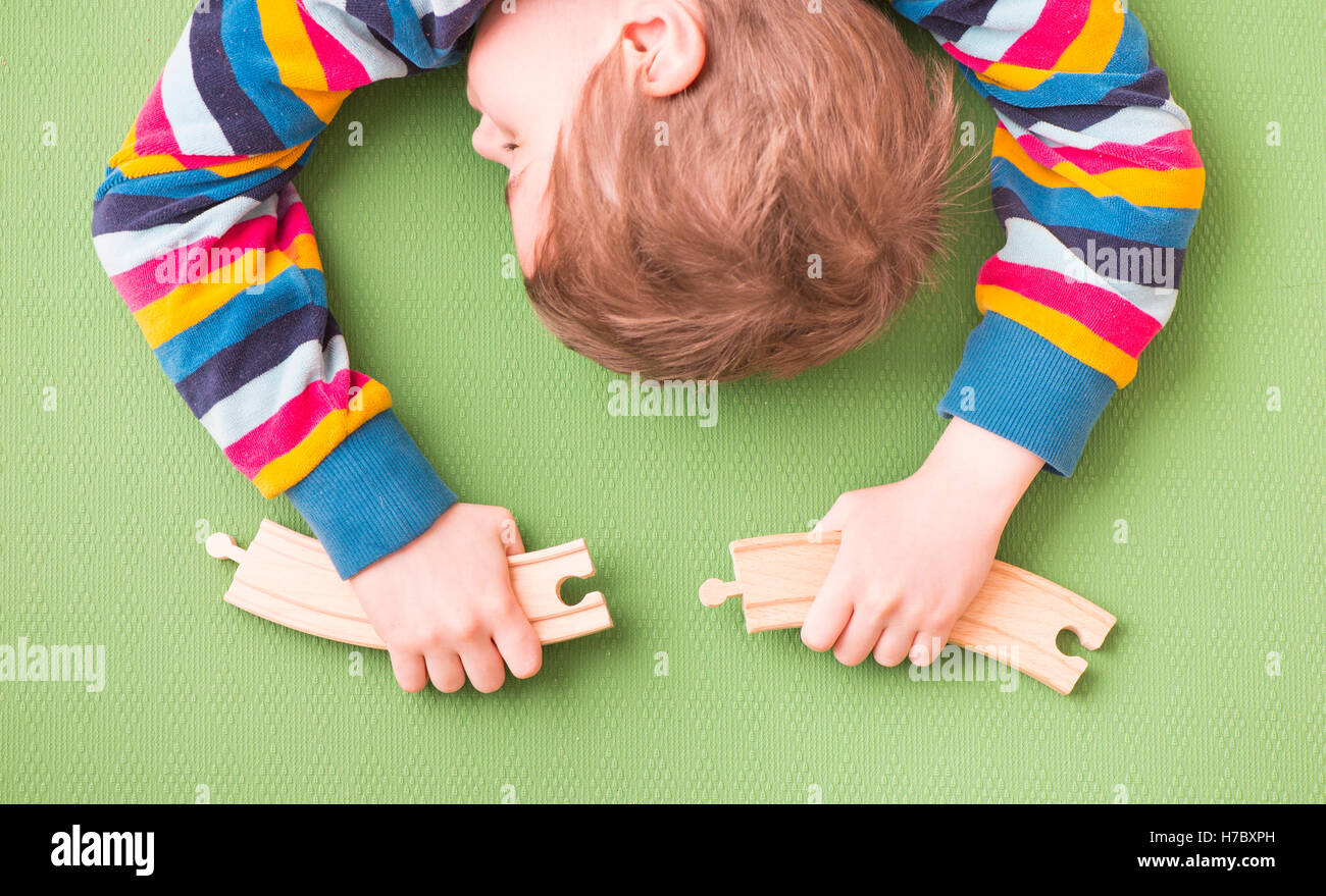 Stanco bambino che dorme mentre si sta giocando con il giocattolo di legno i binari della ferrovia. Concetto di infanzia di apprendimento e di creatività. Foto Stock