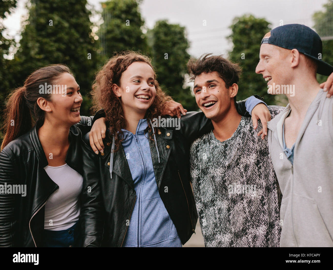 Ritratto di gruppo multirazziale di persone godendo all'esterno. Quattro giovani amici in piedi insieme e sorridente. Foto Stock