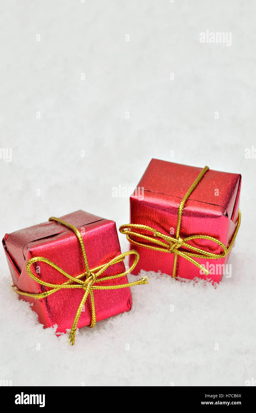 Due piccoli rosso metallico parcelle luminoso sulla neve sfondo, vicino, spazio per il testo, verticale Foto Stock