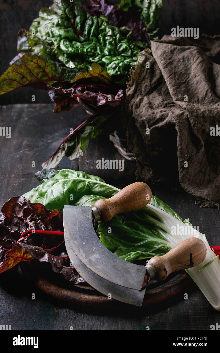 Varietà di bietole novelle mangold foglie di insalata woode sul tagliere con coltello vintage e cilicio rag oltre il vecchio legno scuro ba Foto Stock
