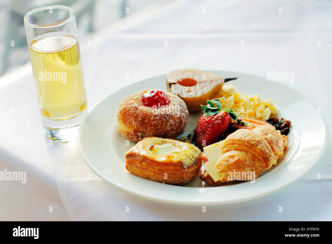 Un assortimento di pasticceria e una fragola su un piatto bianco con un bicchiere di succo di frutta Foto Stock