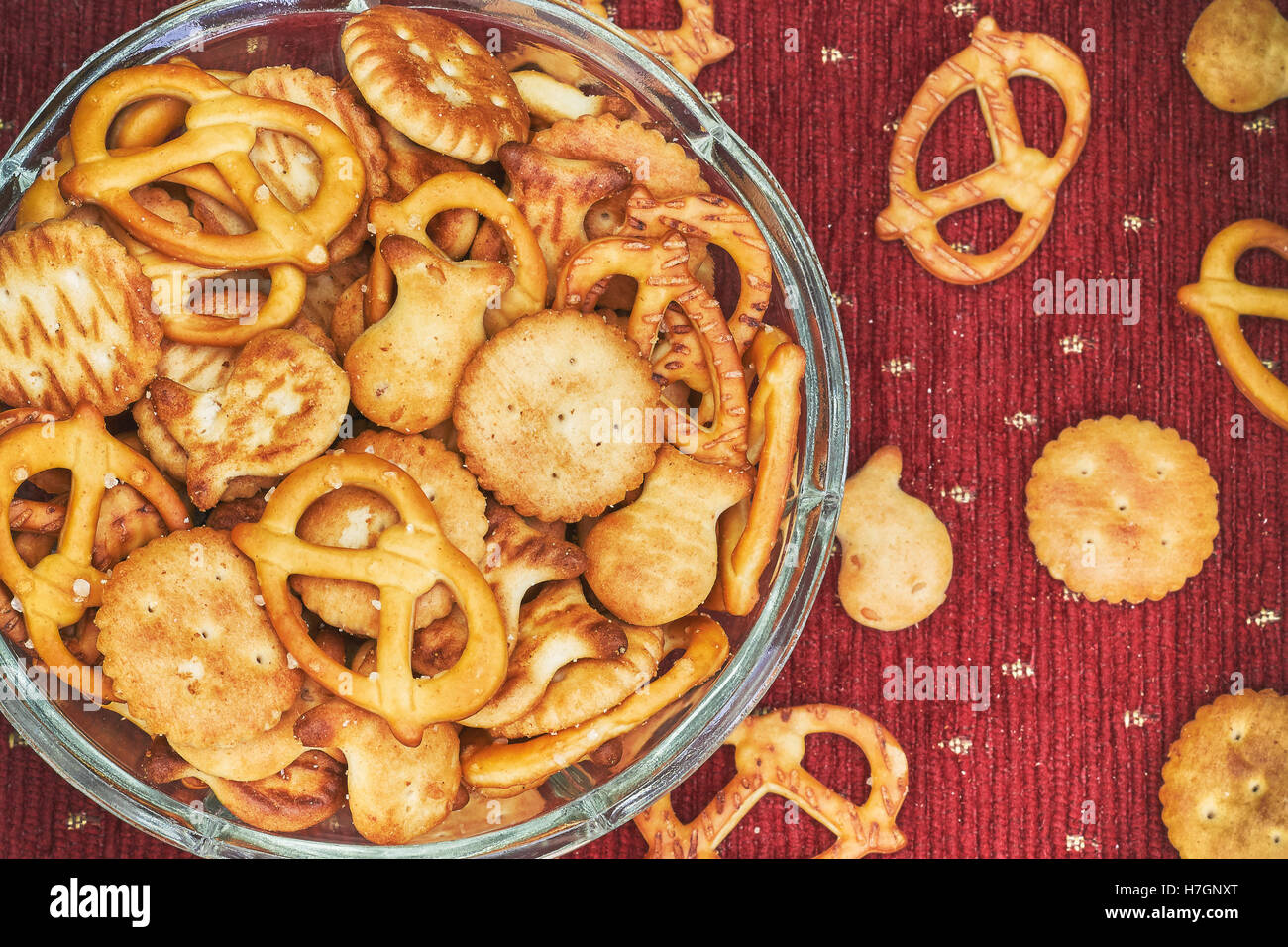 Mix di snack salati (cracker e salatini) in recipiente di vetro su sfondo rosso Foto Stock