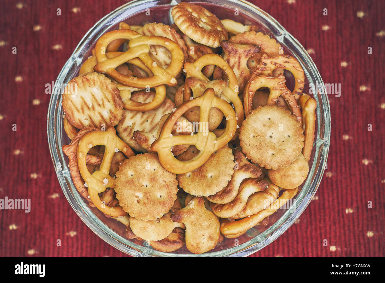 Mix di snack salati (cracker e salatini) in recipiente di vetro su sfondo rosso Foto Stock