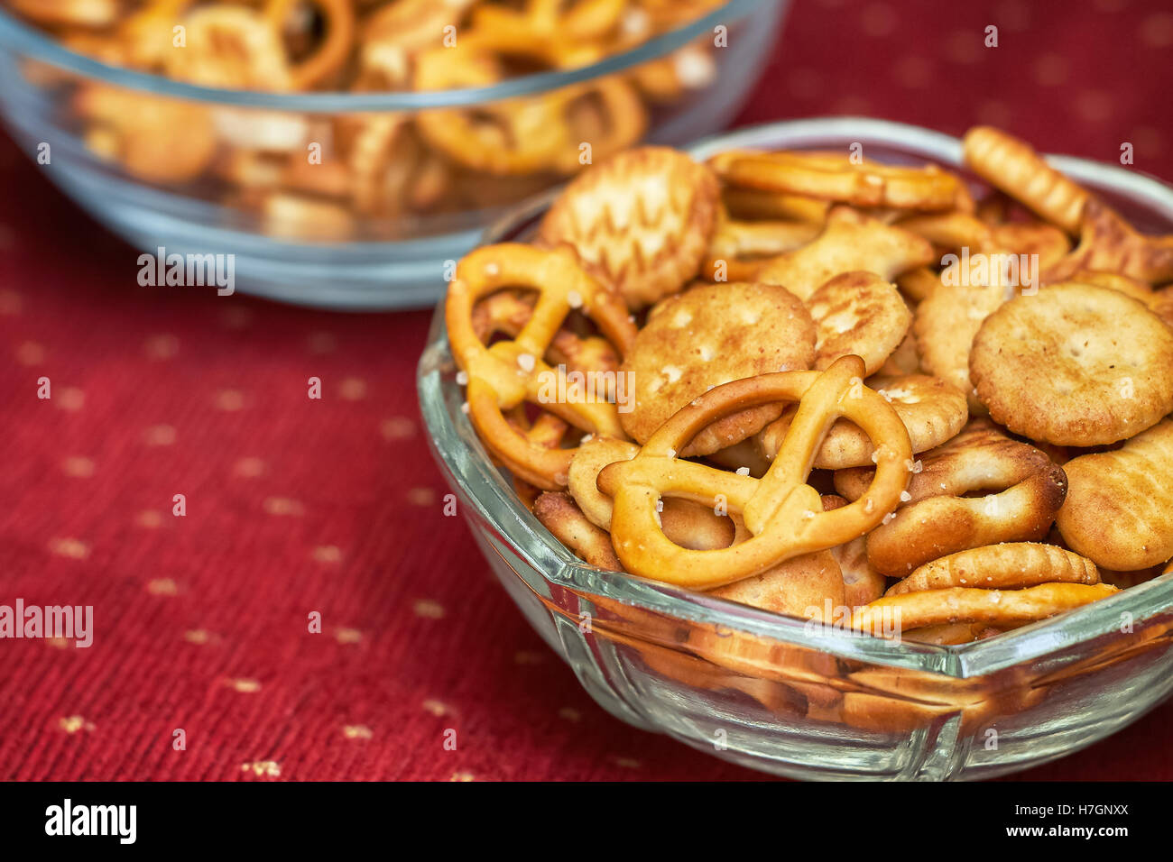 Mix di snack salati (cracker e salatini) in recipiente di vetro su sfondo rosso Foto Stock