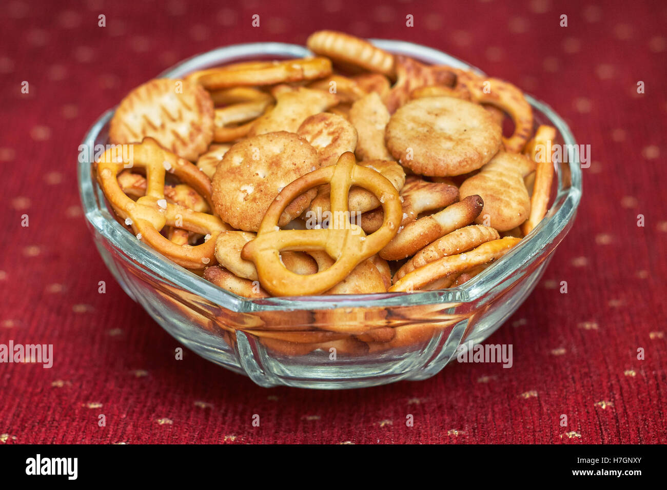 Mix di snack salati (cracker e salatini) in recipiente di vetro su sfondo rosso Foto Stock