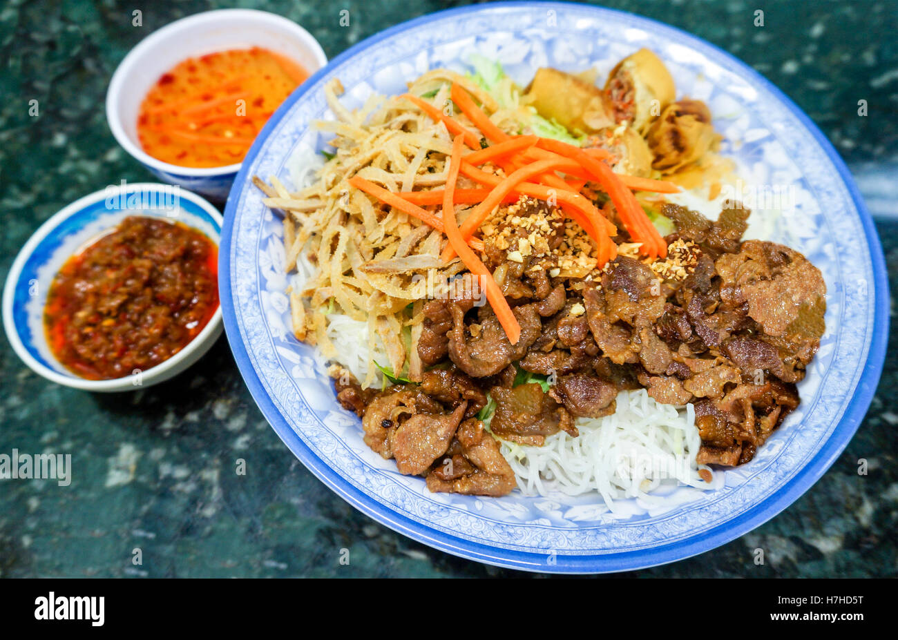Ciotola tradizionale di vietnamiti bun vermicelli riso stick a base di noodle con insalata di carne charbroiled, shredded carne di maiale, fritte ro a molla Foto Stock