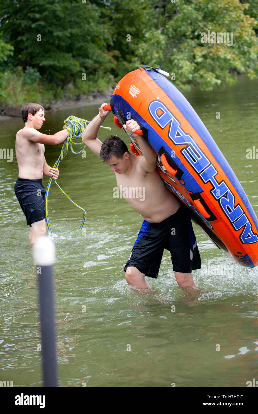 Teen boys portando in Airhead fetta Super Sport d'acqua e tubo di avvolgimento della fune di traino dopo una grande corsa. Clitherall Minnesota MN USA Foto Stock