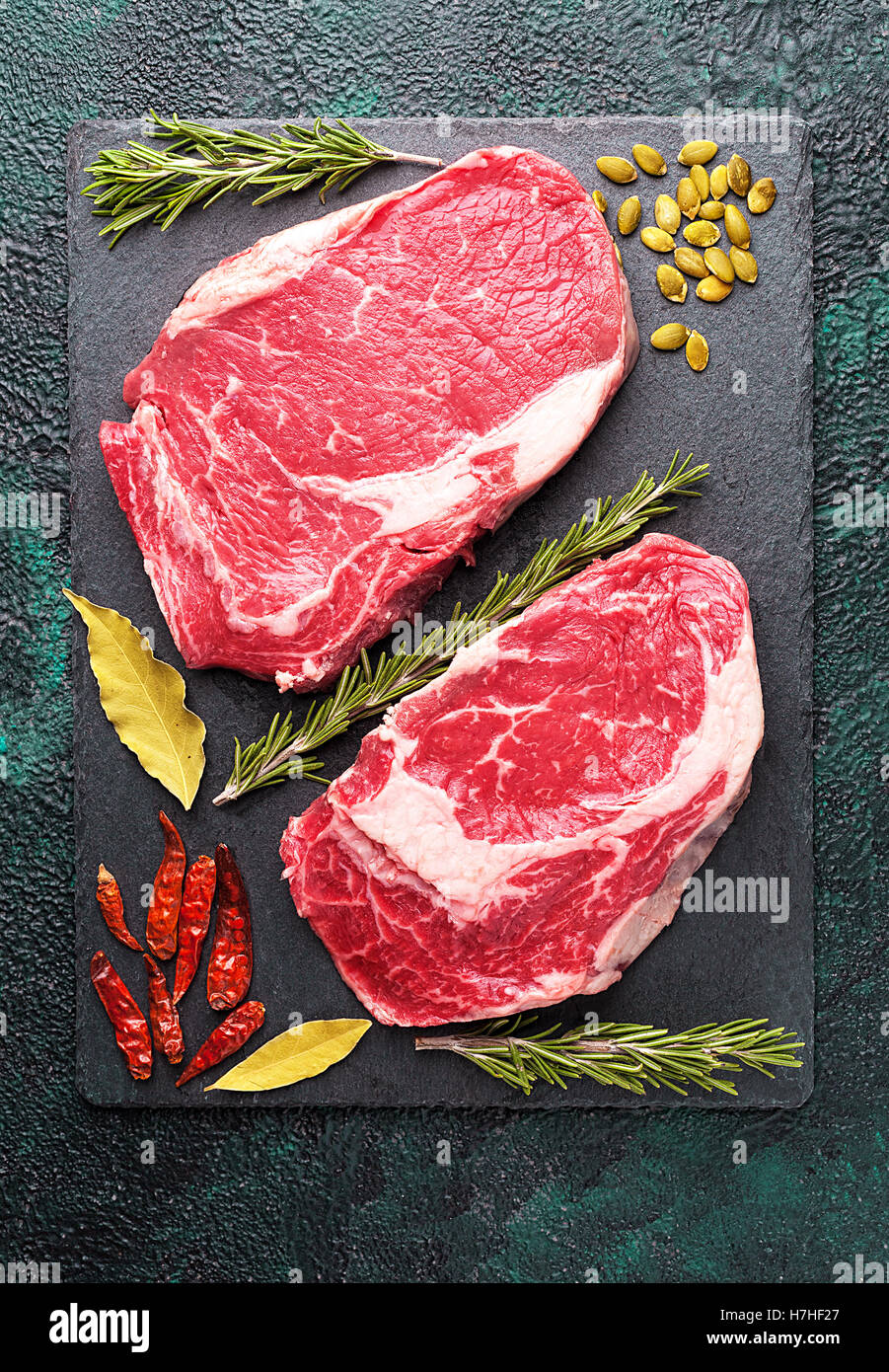 Due pezzi di carne cruda di manzo su una piastra di ardesia con rosmarino Foto Stock
