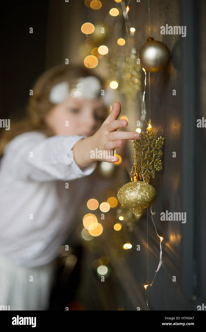I migliori Auguri di Buon Natale. Ragazza di 8-9 anni in bianche vesti con delizia tocca oro ghirlande di Natale e ornamenti. Essi brillare un m Foto Stock