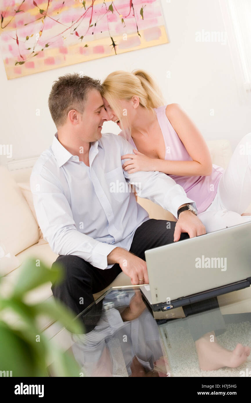 Paio di ridere mentre è seduto con un computer portatile su un divano in soggiorno Foto Stock