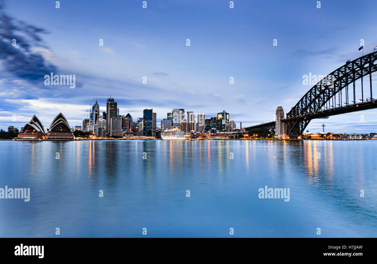 La città di Sydney CBD landmarks attraverso Harbou da case a ponte ad arco ora blu del tramonto quando le luci riflettono ancora in acque Foto Stock