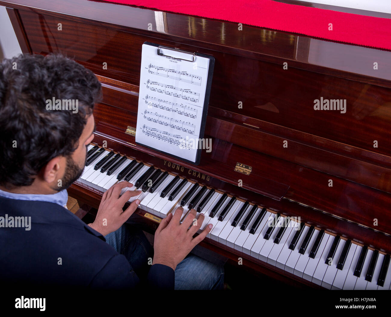 L'uomo suonare il piano utilizzando note durante la seduta, ragazzo suonare il pianoforte con seduta e panno rosso sul pianoforte Foto Stock