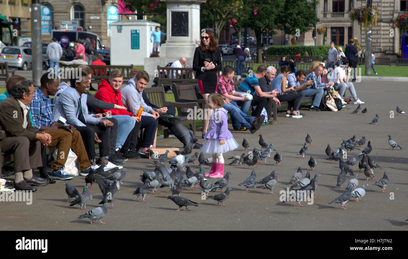 I turisti e i locali godono di bambina gioca con piccioni in George Square Foto Stock