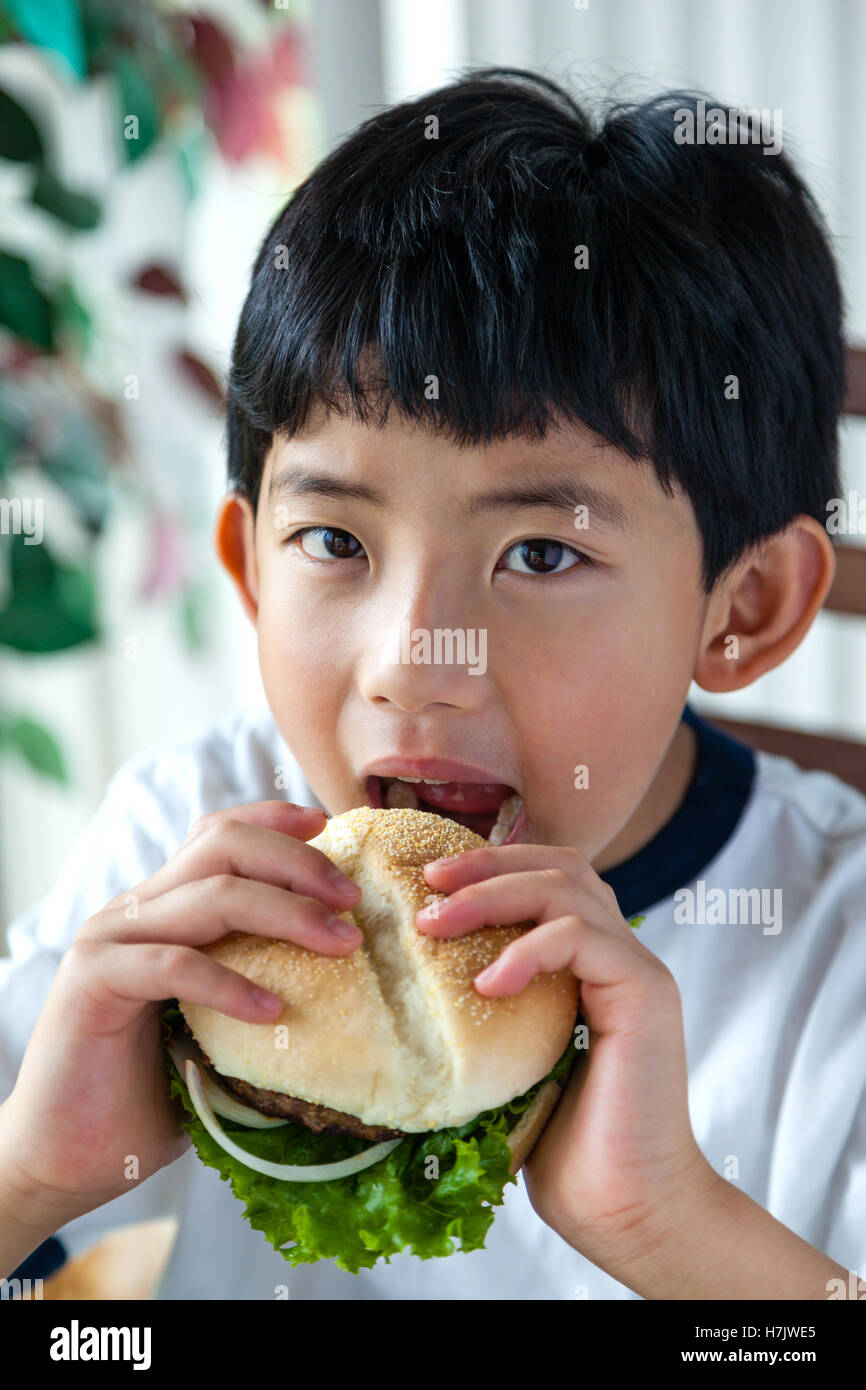 Ragazzo asiatico prendendo un morso sul suo burger. Foto Stock