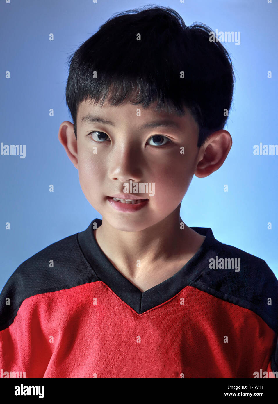 Ragazzo asiatico che indossa una maglia sportiva in posa di studio, con illuminazione speciale per un lato. Isolato su sfondo blu Foto Stock