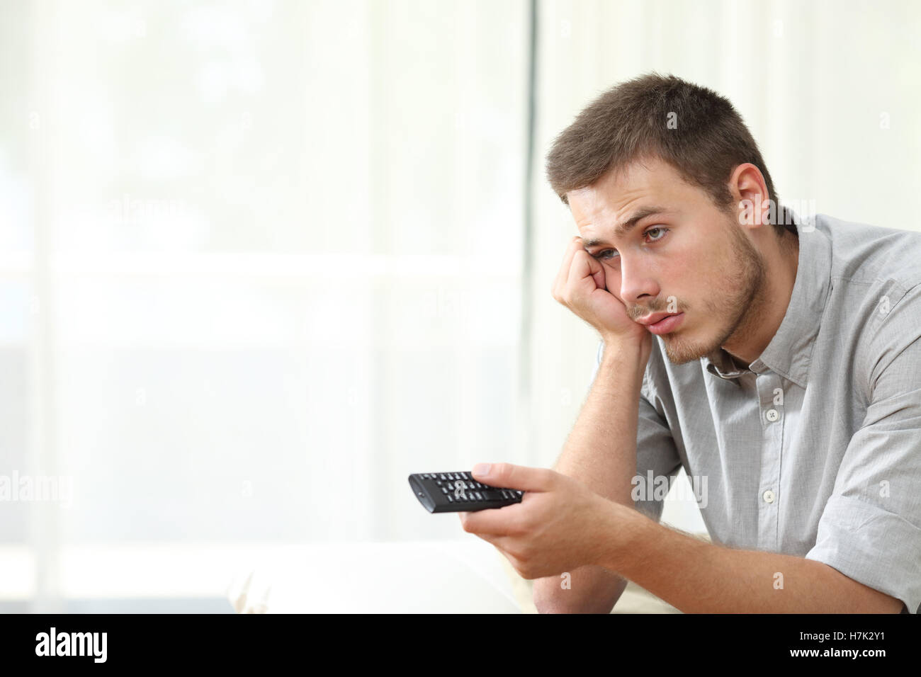 Annoiato uomo guarda la TV e lo zapping seduto su un divano a casa Foto Stock