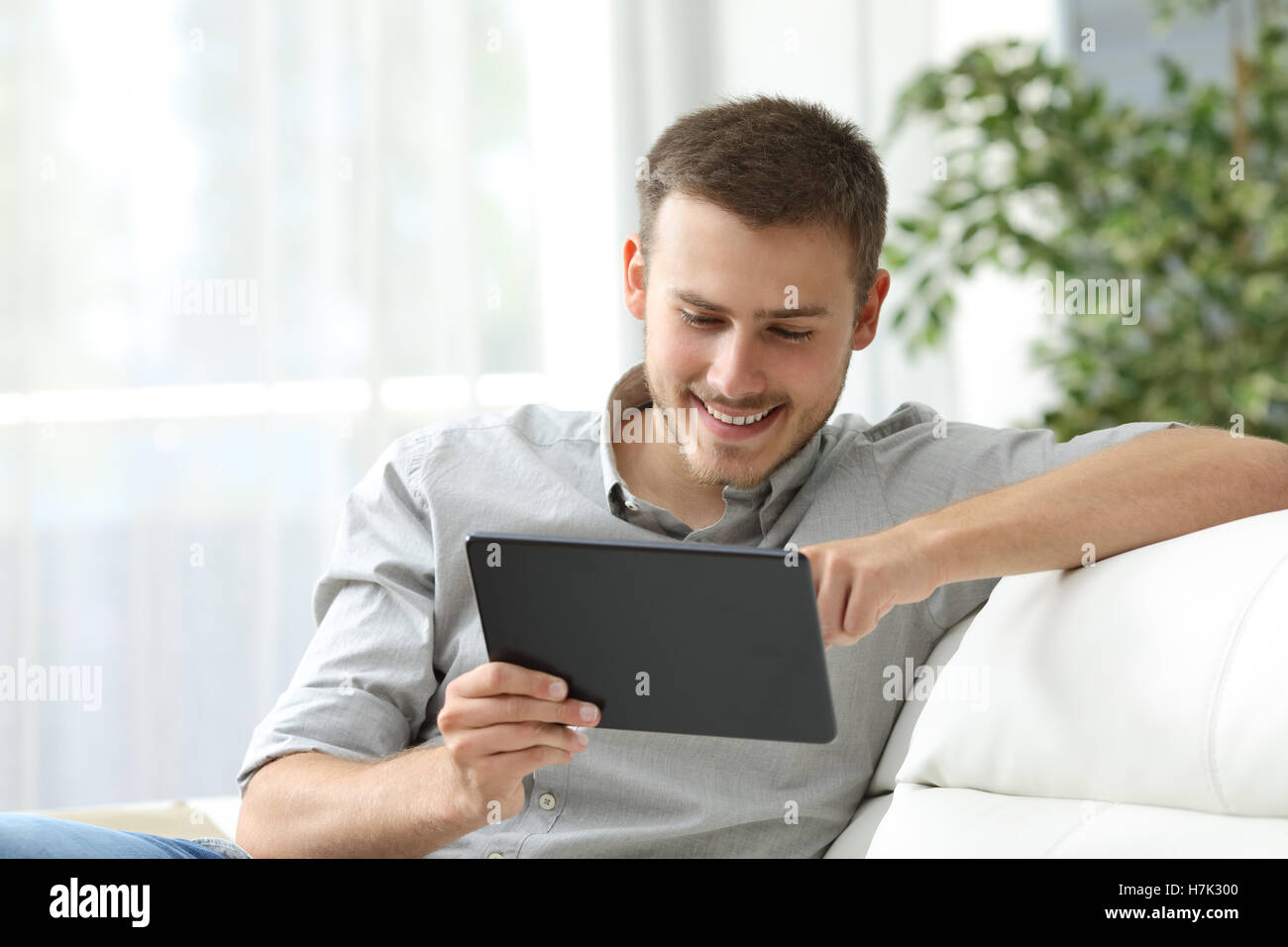 Uomo felice navigando in un tablet seduto su un divano a casa Foto Stock