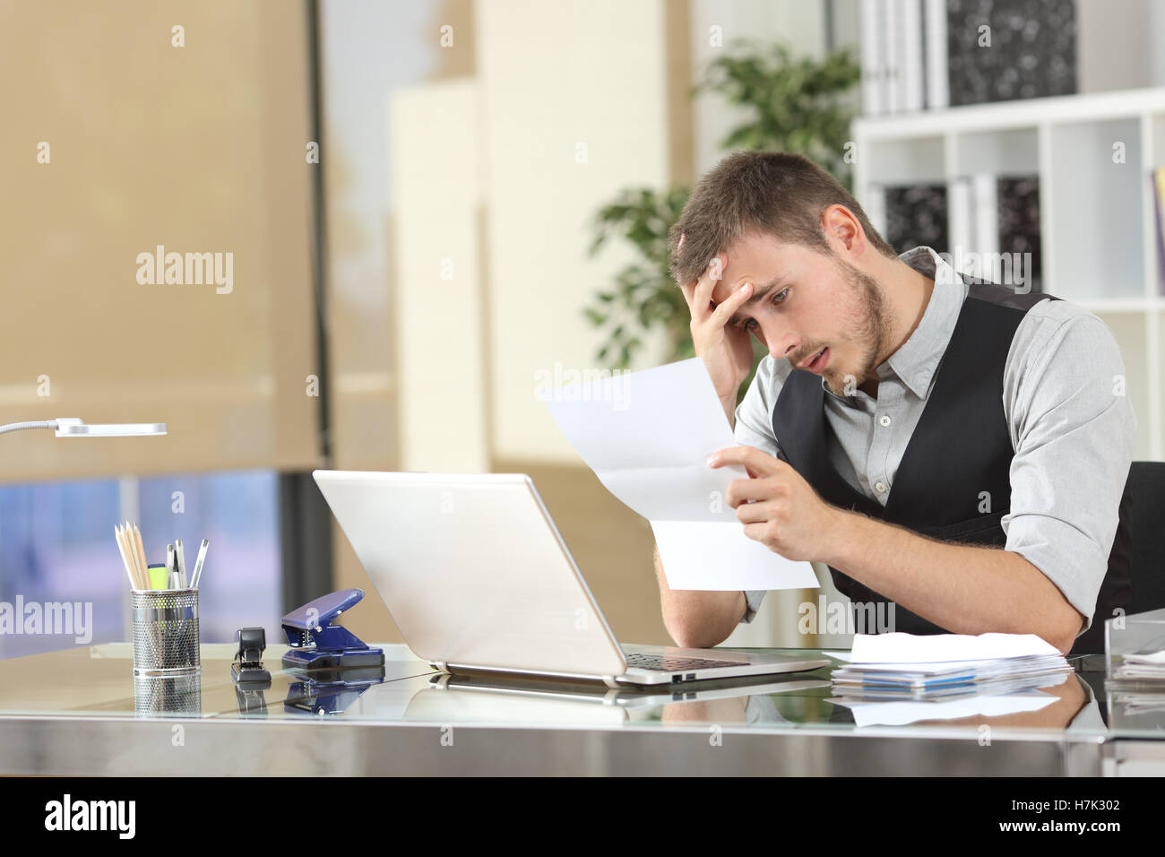 Imprenditore triste la lettura di cattive notizie in una lettera seduto in una scrivania in ufficio Foto Stock
