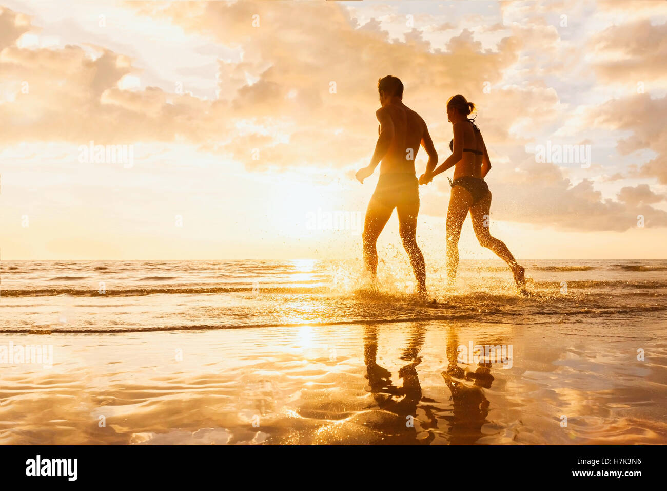 Felice allegro giovane divertendosi in esecuzione al mare insieme e fare schizzi di acqua su una spiaggia tropicale al tramonto luna di miele Foto Stock