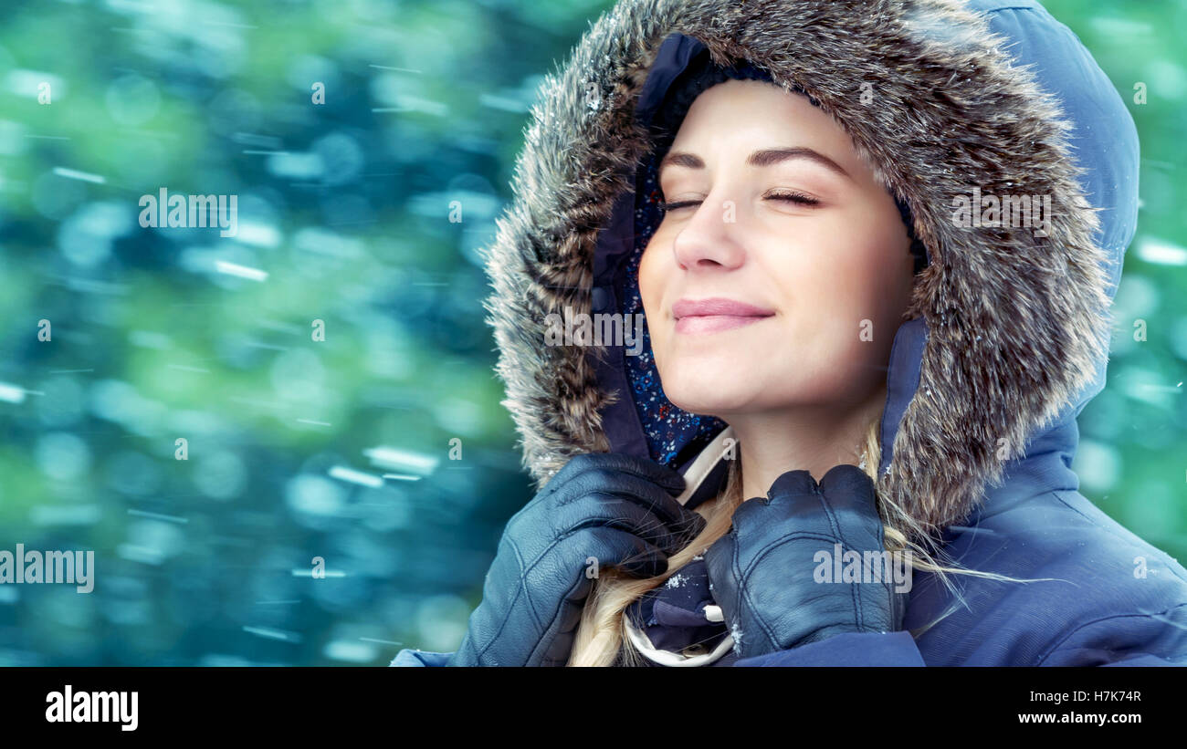 Ritratto di una bella ragazza in winter park, con gli occhi chiusi godendo di caduta di neve, indossa una giacca calda con cappa di pelliccia, felice inverno Foto Stock