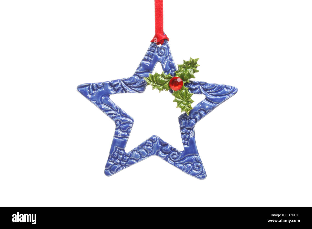 Ceramica Blu stella di Natale con ceramica Holly foglie e un gioiello a bacca rossa appesa a un nastro rosso isolata contro bianco Foto Stock