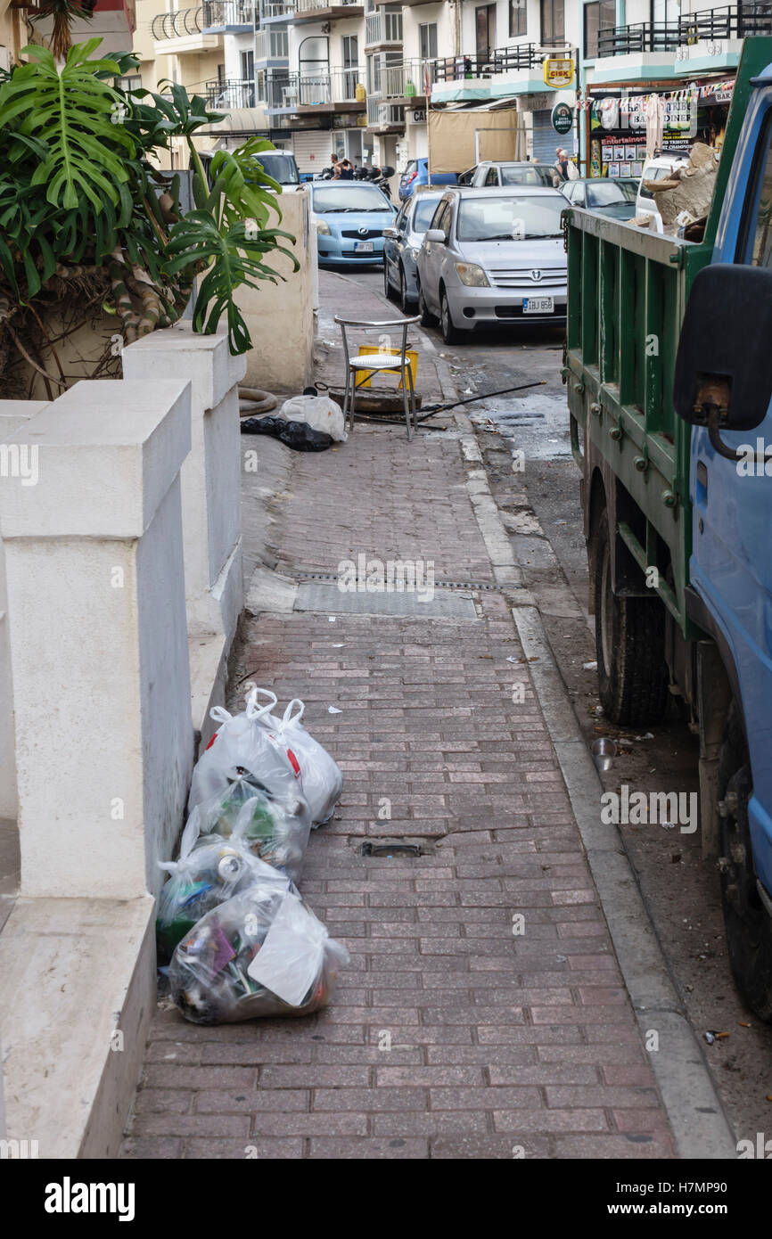 Malta, strade - Qawra. Blocchi di lettiera il marciapiede con un drain aperto e aste di fognature oltre. Foto Stock