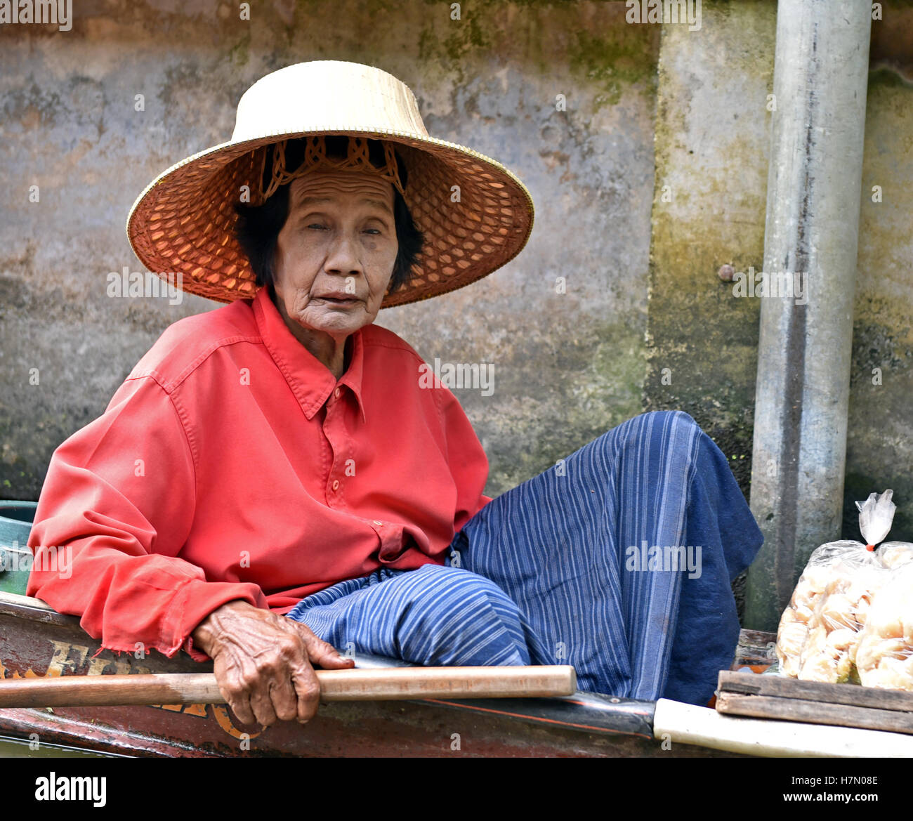 Una vecchia signora pagaie la sua canoa, attraverso i canali di vendita di alimenti al Mercato Galleggiante di Damnoen Saduak vicino a Bangkok in Tailandia Foto Stock