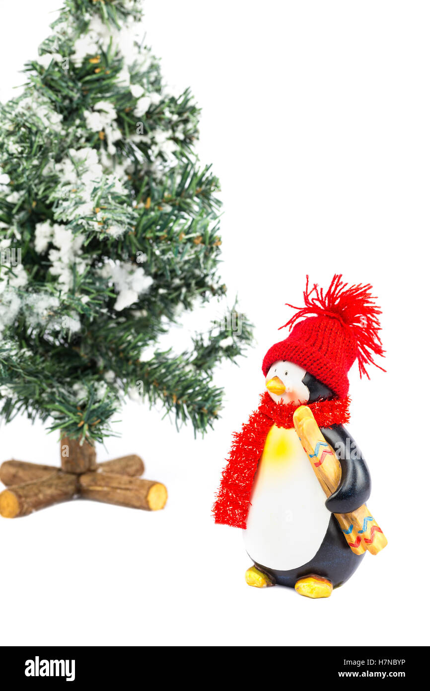 Penguin figurine con cappuccio rosso scialle sci e albero di natale su sfondo bianco Foto Stock