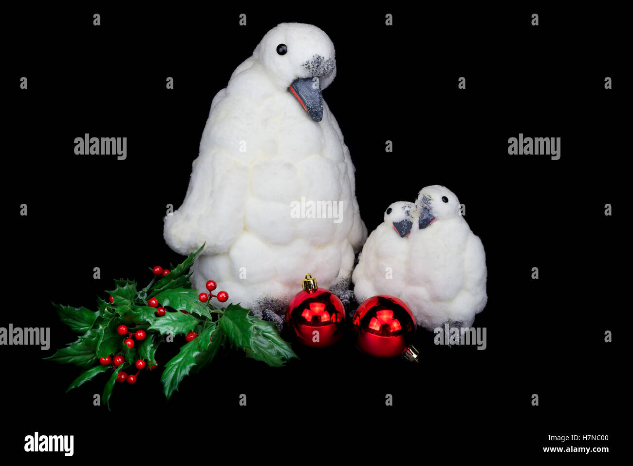 Penguin figure come famiglia con baubles e holly bacche su sfondo nero Foto Stock