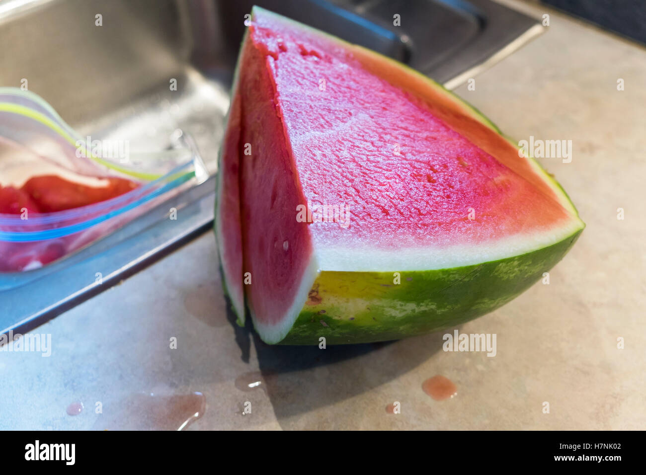 Fette di fresco cocomero senza semi essendo tagliato su un bancone cucina e lavello. Foto Stock