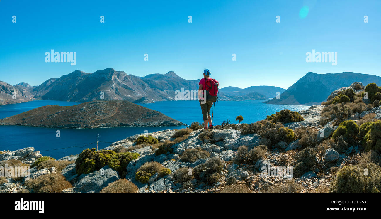 Figura femminile in rosso affacciato sul mare e sulle isole, con cielo blu, Emborios Bay, Kalymnos Foto Stock