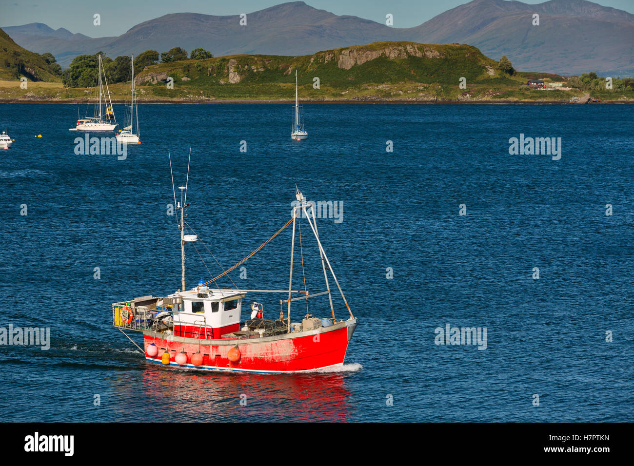 Isola Kerrera vista con le navi a vela. Rosso barca dei pescatori di fronte. Foto Stock