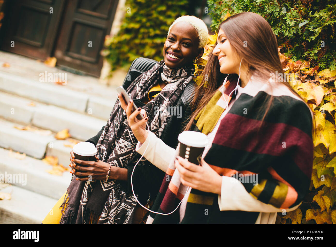 Americano africano e caucasici che pongono la donna fuori con il telefono cellulare e una tazza di caffè per andare in autunno Foto Stock