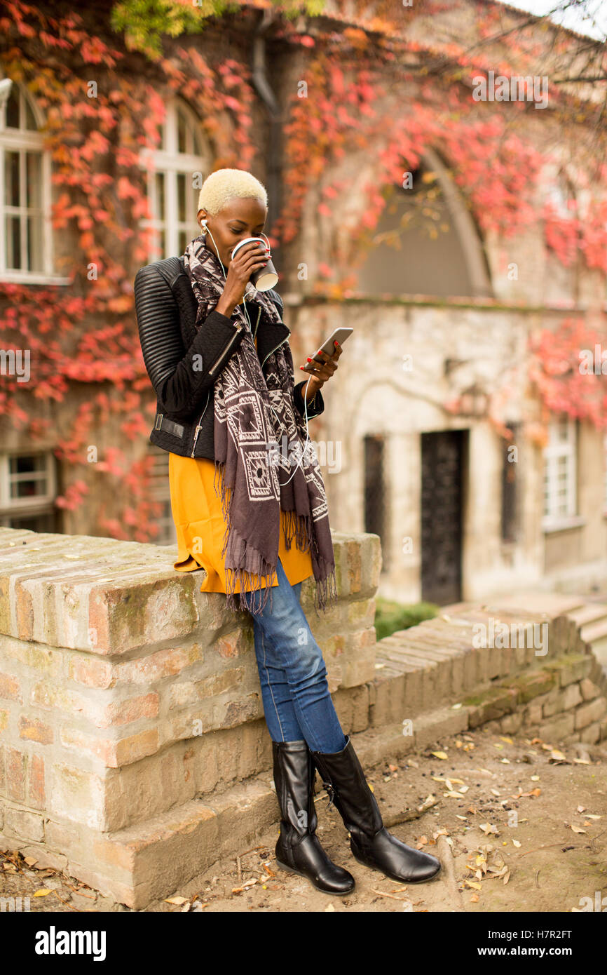 Moderno e giovane africano donna americana in posa con caffè di andare e il telefono cellulare all'aperto Foto Stock